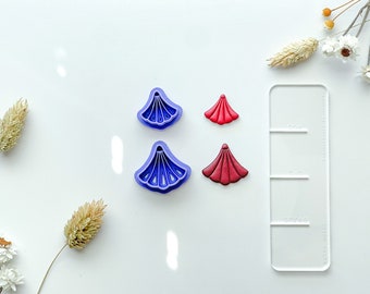 May include: Two purple plastic flower cutters and two red fondant flower shapes on a white surface.