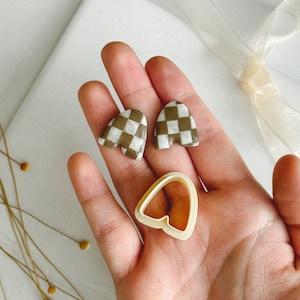 May include: A pair of brown and white checkered heart-shaped earrings and a heart-shaped cookie cutter.