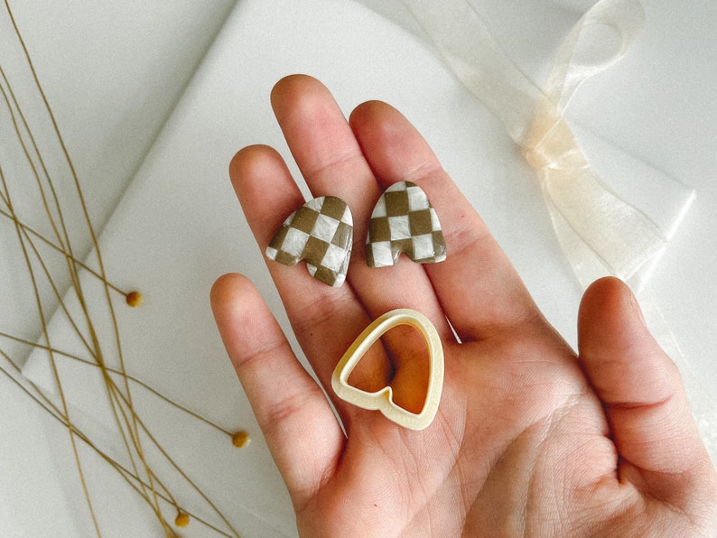May include: A pair of brown and white checkered heart-shaped earrings and a heart-shaped cookie cutter.