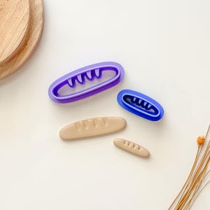 May include: Three purple and blue plastic cookie cutters shaped like baguettes, and two beige clay baguettes.