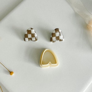 May include: A pair of checkerboard patterned earrings in brown and white, with a single cream-colored earring mold.