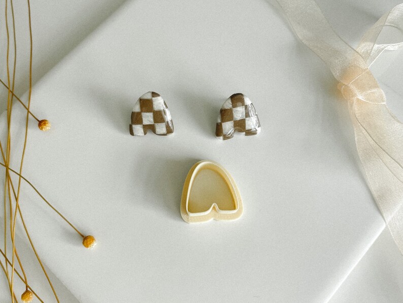 May include: A pair of checkerboard patterned earrings in brown and white, with a single cream-colored earring mold.
