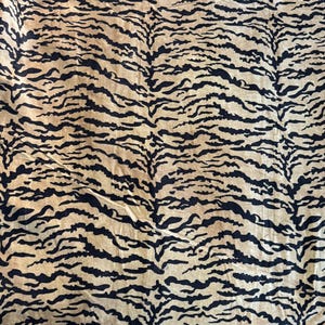 May include: A textile with a tiger stripe pattern. The fabric features black stripes on a tan background. The stripes are irregular and mimic the natural markings of a tiger. The fabric appears to be soft and pliable.