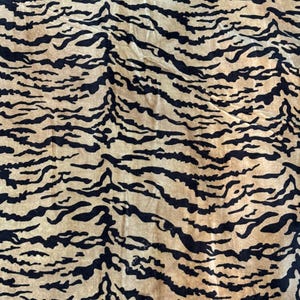 May include: Close-up of a fabric with a tiger stripe pattern. The background is a light tan color, and the stripes are black. The fabric has a soft, textured appearance. The pattern is a repeating design.