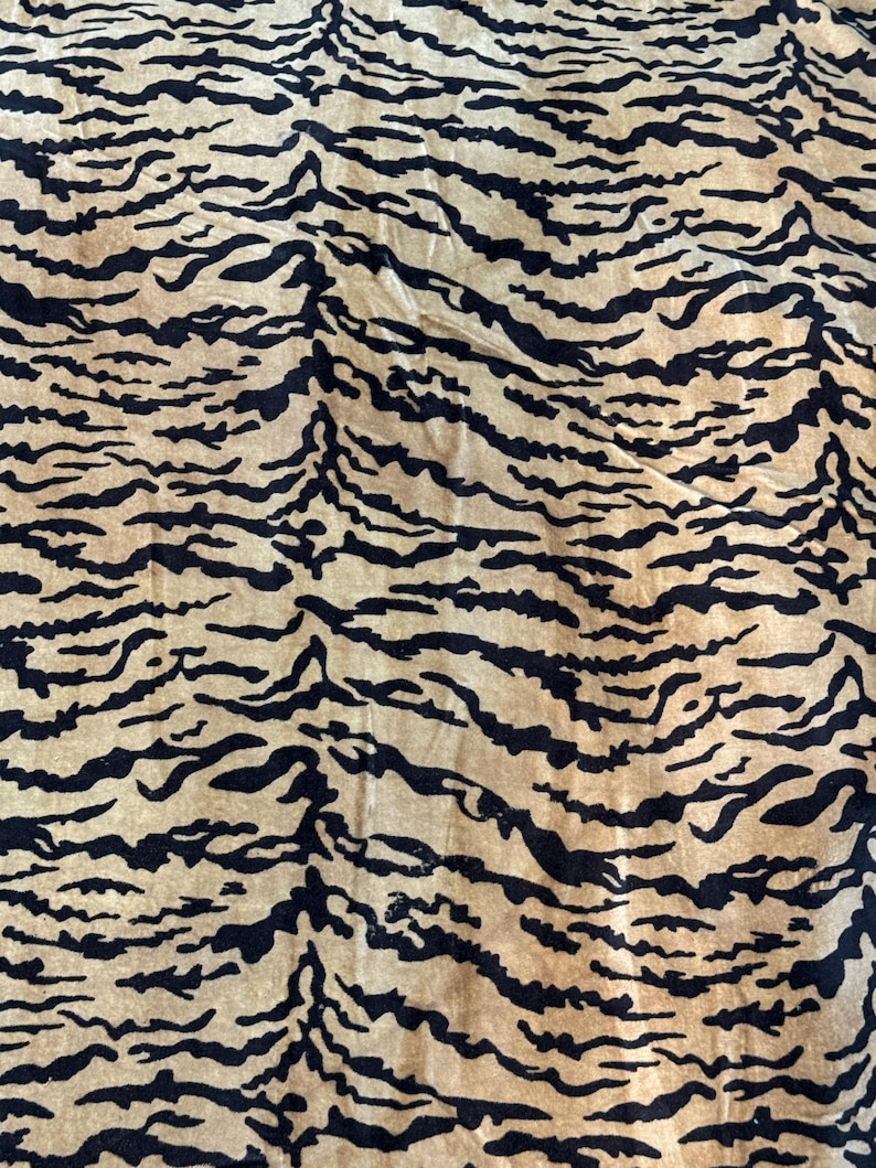 May include: Close-up of a fabric with a tiger stripe pattern. The background is a light tan color, and the stripes are black. The fabric has a soft, textured appearance. The pattern is a repeating design.
