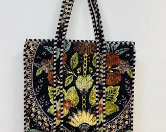 May include: A black tote bag with a floral pattern in shades of green, brown, and pink. The bag has a black and white striped trim and a black handle.