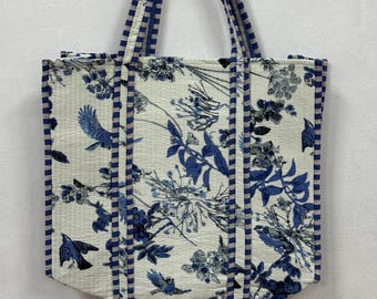 May include: A white tote bag with blue and white striped handles and a floral print featuring blue birds and flowers.