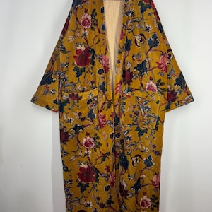 May include: Mustard yellow floral print kimono-style robe with a striped interior. The robe features a large floral pattern in shades of red, pink, and blue. It has two front pockets and long sleeves.