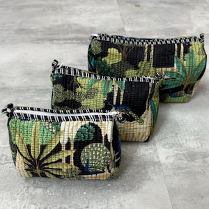 May include: Three quilted cosmetic bags with a tropical leaf and peacock feather pattern in shades of green, black, and cream. Each bag has a black and white striped zipper trim and a zipper closure.