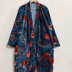 May include: A long, teal velvet robe with a floral pattern in red, pink, and gold. The robe has two pockets and a striped blue and white lining. It is hanging on a wooden hanger.
