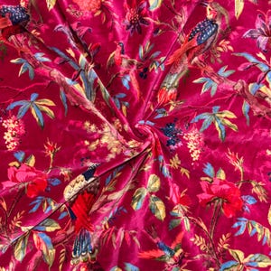 May include: A vibrant, fuchsia-colored fabric with a detailed floral and bird pattern. The design features colorful birds perched among blooming roses, leaves, and branches. The fabric has a soft, velvety texture.