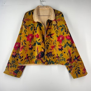 May include: A reversible jacket with a floral and bird pattern in shades of gold, red, and green. The jacket has a striped collar and cuffs. The jacket is hanging on a metal hanger.