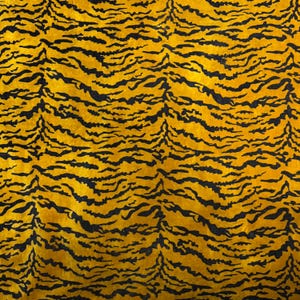 Puede incluir: Primer plano de una tela con estampado de rayas de tigre. La tela tiene un fondo amarillo con rayas negras. Las rayas son onduladas e irregulares, creando una apariencia texturizada. El patrón recuerda a un estampado animal.