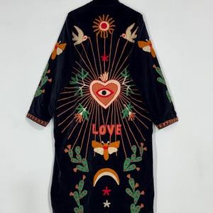 May include: Black velvet coat with colorful embroidered design. Features a heart with an eye, sun, birds, cacti, and the word "LOVE". The coat has long sleeves and a mandarin collar.