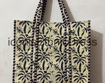 Può includere: Borsa tote trapuntata con sfondo crema e motivo ripetuto di palme nere. La borsa ha manici e finiture a righe nere e rosa. La borsa è rettangolare e ha un design semplice.