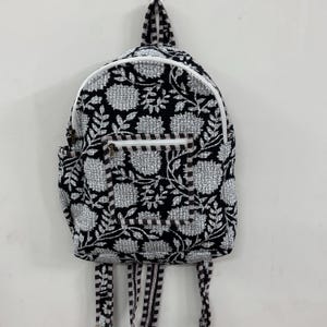以下が含まれることがあります： 白と黒の花柄プリントのバックパック。白いジッパーとトリムが付いています。バックパックにはフロントポケットと調節可能なストラップが付いています。バッグの高さは約40cm、幅は約30cmです。