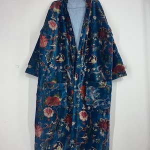 Puede incluir: Bata larga con frente abierto, con un estampado floral en color verde azulado. La bata de terciopelo presenta diseños florales rojos y crema. El forro interior es de tela a rayas azul claro y blanco. Dos bolsillos son visibles en la parte delantera.