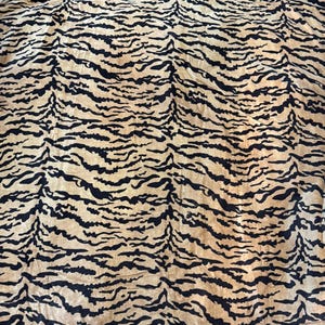 Pode incluir: Um tecido com um padrão de listras de tigre. O material apresenta faixas alternadas de preto e castanho claro, criando um padrão arrojado. O tecido parece macio e fluido, adequado para vários usos.