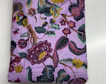 May include: Folded fabric with a floral design. The pattern includes large, dark burgundy flowers, green leaves, and yellow accents on a light purple backdrop. The material is likely cotton or a similar fabric.