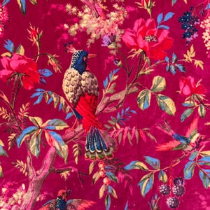 May include: A vibrant fabric featuring a detailed floral and bird pattern. The design showcases colorful birds perched on branches amidst large pink roses, blue and green leaves, and other flowers, all set against a deep magenta background.