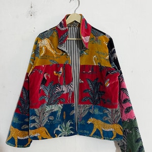 Pode incluir: Um casaco de manga comprida com um design de patchwork em tecido de veludo com vários estampados de animais e plantas tropicais em tons de amarelo mostarda, vermelho, azul e verde. O forro interior apresenta um padrão de riscas verticais pretas e brancas.