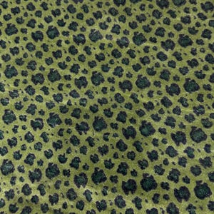 Peut inclure: Gros plan sur un tissu vert avec un motif léopard. Le tissu a une texture douce et veloutée. Les taches de léopard sont vert foncé et de forme irrégulière, dispersées sur le fond vert clair.
