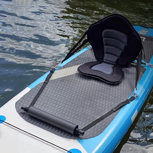 Puede incluir: Un asiento de kayak negro y gris con correas ajustables está sujeto a una tabla de paddleboard azul y blanca. El asiento tiene respaldo y cojín acolchados. Una manija negra está en la parte delantera de la tabla.