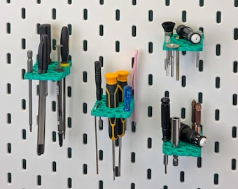 May include: Green 3D-printed tool organisers holding screwdrivers, bits, and small tools. The organisers are mounted on a white pegboard, offering tidy storage for a workshop or craft space. The tools are neatly arranged.