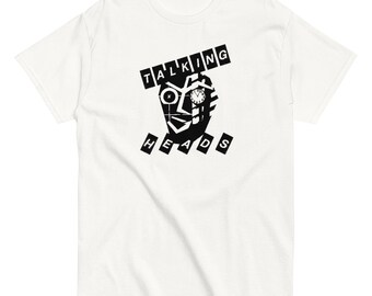 May include: White t-shirt featuring a black and white graphic of a stylized face with a clock and the words "TALKING HEADS" above and "HEADS" below the face. The shirt has short sleeves and a crew neck.