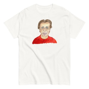 Könnte beinhalten: Ein weißes T-Shirt mit einer Cartoon-Illustration eines Mannes mit braunen Haaren, der ein rotes Hemd und eine Brille trägt. Der Mann hat ein breites Lächeln mit sichtbaren Zähnen.