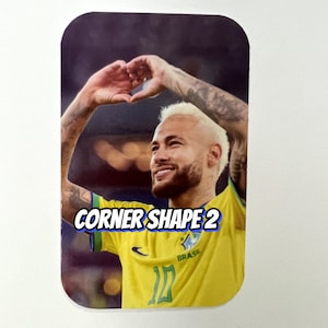 Pu&ograve; includere: Primo piano di un calciatore che indossa una maglia gialla e verde con la scritta "BRASIL" su di essa. Il calciatore sta formando un cuore con le mani e sorride. Il testo "CORNER SHAPE 2" &egrave; visibile nell'immagine.