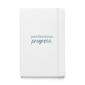 Puede incluir: Un cuaderno blanco con las palabras "perfection" y "progress" en escritura turquesa. El cuaderno tiene un cierre de banda elástica a juego. La portada es limpia y minimalista.