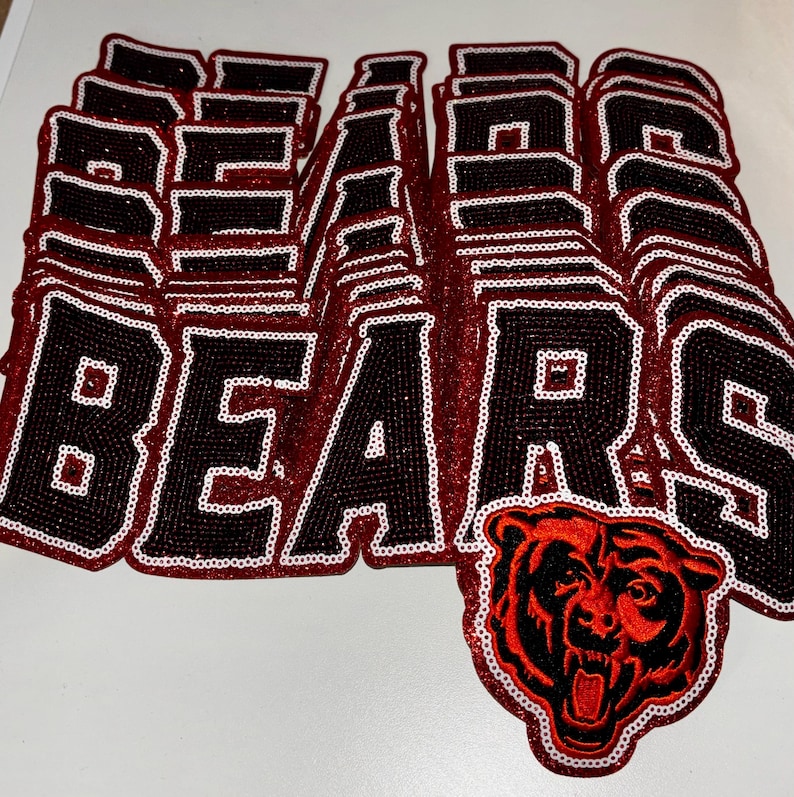 May include: A collection of stacked fabric patches featuring the word BEARS in black block letters with a white sequin border. One patch at the bottom right includes a detailed embroidered graphic of a snarling bear head in red and black.
