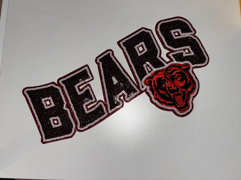 May include: A decorative patch featuring the word BEARS in black sequins with a white sequin outline. The letter R is partially replaced by a red and black embroidered bear head graphic with an open mouth, also outlined in white sequins.