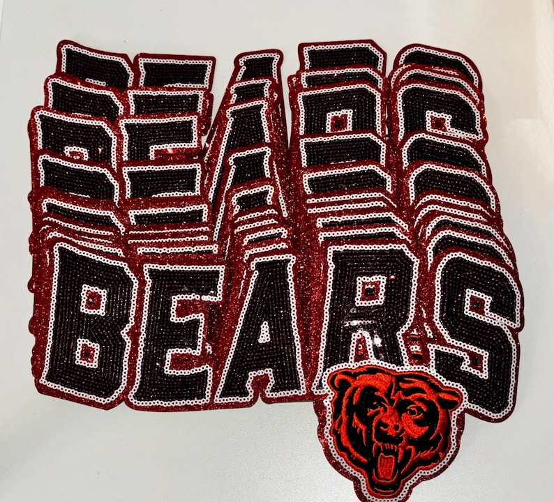 May include: A stack of multiple iron-on patches featuring the word BEARS in black block letters with a white outline and a red glitter border. The bottom patch includes a detailed graphic of a roaring bear head in red and black glitter.