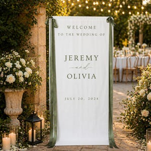 May include: A tall white rectangular fabric wedding welcome sign featuring dark green text that reads Welcome to the wedding of Jeremy and Olivia July 20, 2024. The sign is accented with long dark green ribbons tied at the top corners.