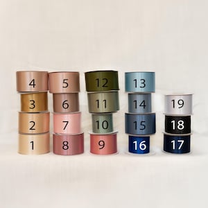 May include: A collection of stacked spools of satin ribbon in various colors, including shades of gold, pink, green, blue, and black. Each spool is labeled with a number from 1 to 19. The ribbons are arranged on a white background.