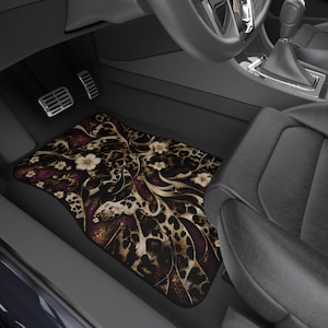 May include: A car floor mat featuring a dark leopard print pattern combined with deep burgundy accents and cream-colored floral motifs. The mat is positioned in the footwell of a vehicle, showing a curved shape that fits the interior floor space.