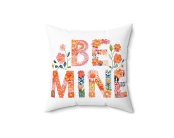 May include: Square white cushion featuring the words "BE MINE" in floral lettering. The letters are filled with flower patterns in orange, pink, and yellow. A decorative cushion for a home interior.