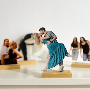 May include: Several wooden photo cutouts of couples in various poses. The main cutout features a couple kissing, the woman in a teal dress. Other cutouts show couples embracing. Each cutout is mounted on a small wooden base.