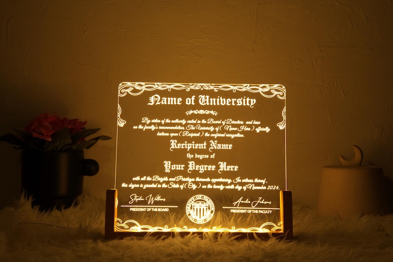 K&ouml;nnte beinhalten: Eine wei&szlig;e, beleuchtete Acrylplakette mit einem dekorativen Rand und dem Text "Name of University" und "Recipient Name" mit dem Abschluss "Your Degree Here". Die Plakette steht auf einem Holzsockel und tr&auml;gt ein Siegel mit dem Text "President of the Board" und "President of the Faculty".