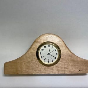 May include: A wooden clock with a gold-colored face and black hands. The clock is set into a wooden base that is shaped like a crescent moon.