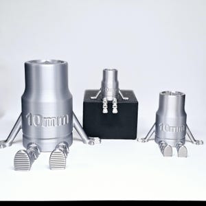 May include: Three silver metal 10mm socket wrenches with legs and feet, the largest is on the left, the smallest is on the right, and the middle wrench is on a black box.