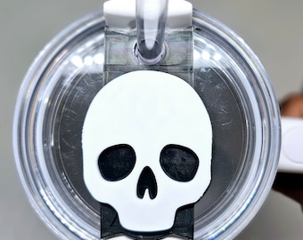 May include: A clear plastic tumbler lid with a white skull-shaped charm attached. The charm has black eyes and a black nose.