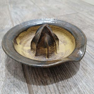 May include: A ceramic citrus juicer with a brown and yellow glaze. The juicer has a pointed center and a wide, shallow base.