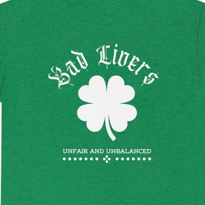 May include: Green t-shirt with a white four-leaf clover and the text "Bad Livers" in a white gothic font. The text "Unfair and Unbalanced" is also in white below the clover.