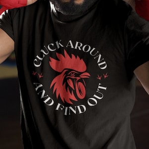 May include: A black t-shirt with a white graphic of a rooster and the text "Cluck Around And Find Out".