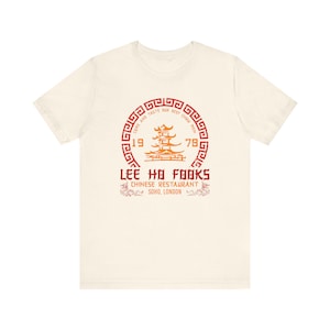 May include: Off-white t-shirt featuring a red and orange circular graphic with the text "LEE HO FOOKS CHINESE RESTAURANT SOHO, LONDON" and the numbers "1978". The graphic includes a pagoda design.