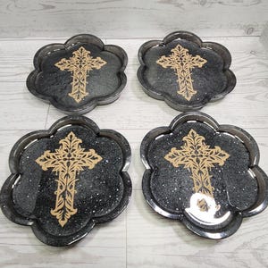 May include: Set of four black and gold coasters with a cross design. Each coaster has a scalloped edge and a glittery finish.