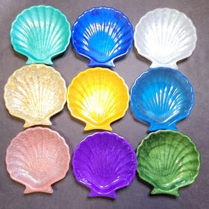 May include: Nine seashell-shaped dishes in various colors, including teal, blue, white, gold, yellow, light blue, pink, purple, and green. Each dish has a textured surface and a scalloped edge, perfect for coastal decor.